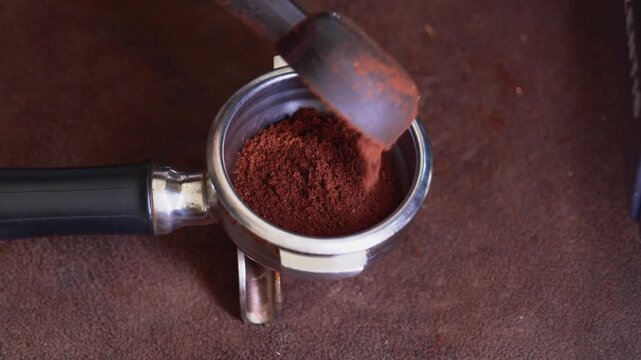 Close-up of freshly ground coffee being poured into an espresso portafilter, preparing for extraction.