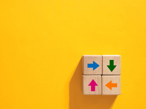 Four wooden cubes showing colorful arrows pointing in different directions on yellow background