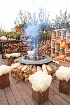 Fire pit in outdoor area surrounded by wooden logs and fresh vegetables on display