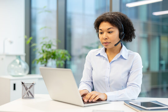Serious and focused young African American woman in headset working in office at laptop