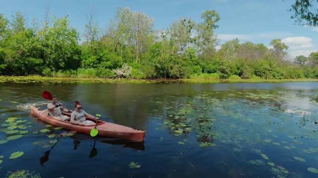 Mature couple paddling a tandem kayak together on a calm river with water lilies promoting active lifestyle