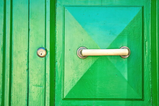 Maniglia moderna e serratura su un portone in legno verde acceso a pannelli