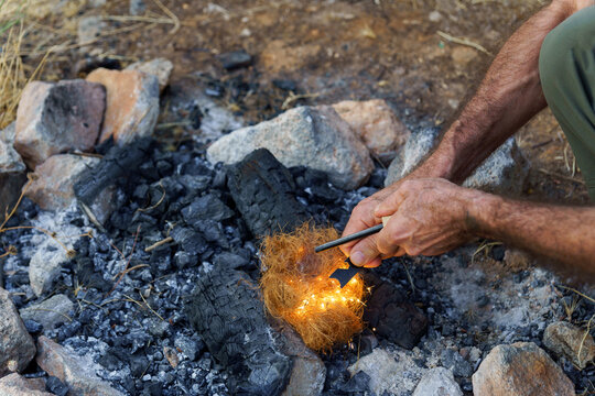 Hands using a ferro rod and striker to create sparks on natural tinder, igniting a flame for a campfire