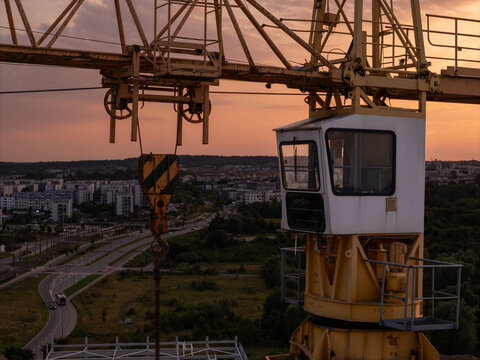 Aerial view of a yellow construction crane with an operator cabin and hook overlooking the city skyline of Gdansk, Poland.