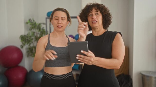 Woman and instructor pointing at tablet and pointing finger while checking poses in a yoga studio; concentration guidance.