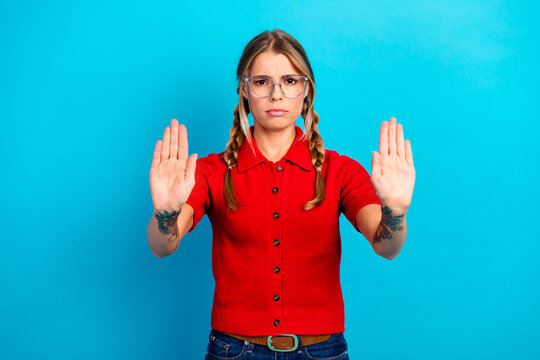 Adorable young woman with braids in a red polo gestures stop against blue background for fashion lifestyle education and shopping promotion
