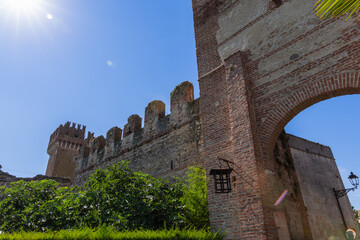 Obraz premium The Scaliger walls of Lazise, Italy, rise above a brick arch, with crenellated towers and warm masonry illuminated by the summer sun.