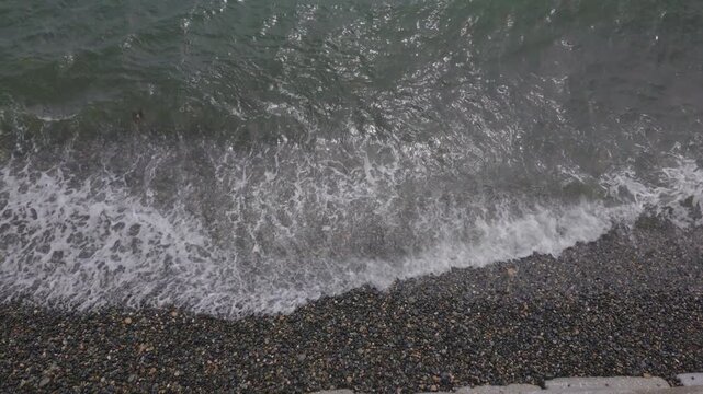 Overhead view of breaking waves at the shoreline of Penzance pebble beach on a hot June day.
