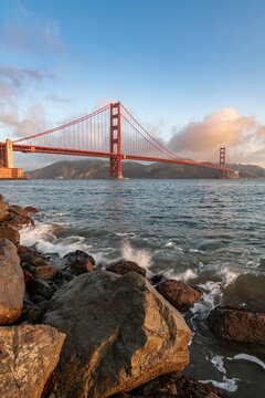 Vertical view of the Golden Gate Bridge at sunrise with rocky shore