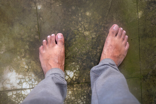 A top-down view of bare human feet standing on a worn concrete floor with natural textures and ample copy space.