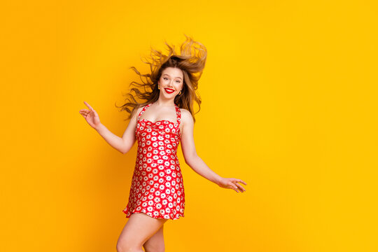 Happy young woman in red daisy dress dancing against bright yellow background smiling with flowing hair playful summer fashion portrait