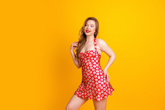 Young woman in red floral dress smiling against a bright yellow background for summer fashion and retro pin-up portrait