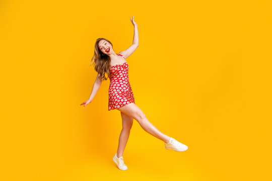Young woman in red floral dress joyfully dancing and smiling against a bright yellow background, playful summer fashion and energetic carefree mood