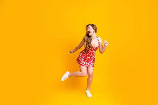 Happy young woman in red floral dress dancing on a bright yellow background expressing joy, energy and summer fashion with casual white sneakers