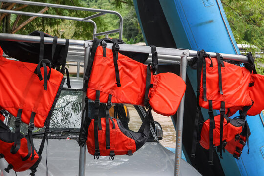 Bright orange life jacket hanging on metal rack above vehicle next to inflatable blue raft, outdoor river rescue gear ready for water adventure