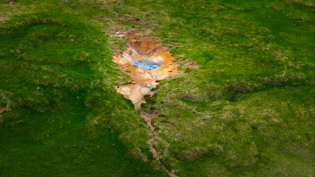 Aerial view of a geothermal hot spring with vibrant mineral deposits surrounded by lush green mossy terrain in the volcanic landscape of Husavik, Nordurthing, Iceland.