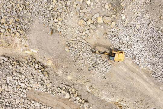 Aerial top down view of a yellow excavator working in a stone quarry, heavy machinery digging rocks in an open pit mine