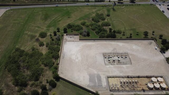 Fenced gas site rests beside busy Wilshire Blvd corridor outside Fort Worth. Storage tanks, equipment layout display energy land use near major thoroughfares in Burleson, Texas