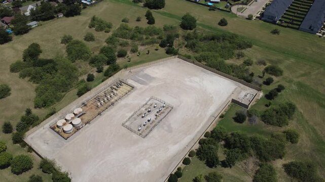 Secured wellhead compound near Wilshire Blvd corridor outside Fort Worth. Tank batteries, processing units illustrate energy land use alongside suburban thoroughfares in Burleson, TX