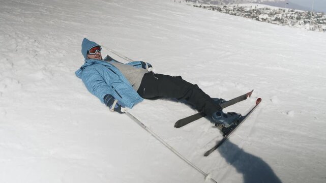 A person helps their friend get up after falling while skiing on a snowy slope. The pair enjoys a winter day at a mountain resort.