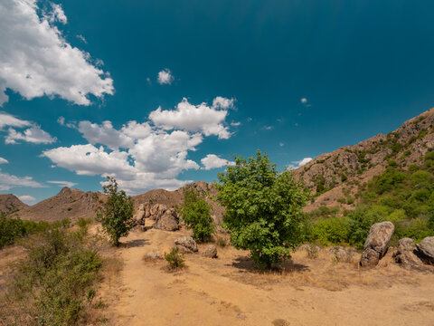 Wide angle shot of the granite monoliths known as Dinosaur Eggs rock formations overlooking arid hills under a cloudy blue sky in Macin Mountains, Dobrogea, Romania.