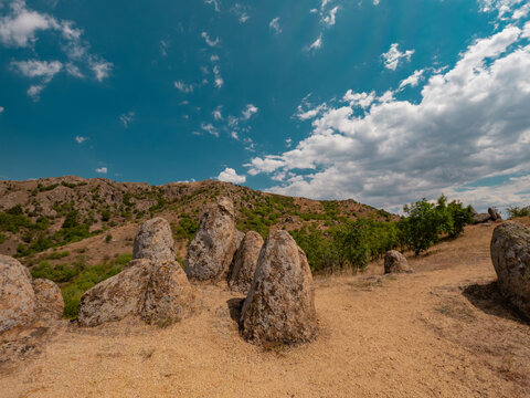 Wide angle shot of the granite monoliths known as Dinosaur Eggs rock formations overlooking arid hills under a cloudy blue sky in Macin Mountains, Dobrogea, Romania.