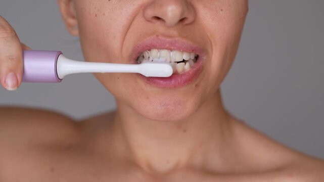 Close-up of young woman using electric toothbrush, demonstrating dental hygiene, oral care and everyday teeth cleaning routine on gray background