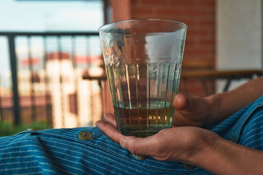 Close-up of a hand holding a ribbed glass with amber drink on a lap