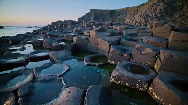 Panning camera revealing hexagonal basalt columns at low tide, exposing terraces and tide pools