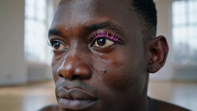 Framing shirtless man wearing bright pink false eyelash on right eye while blinking in loft