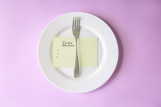 Empty plate with a fork and handwritten diet checklist on a pink studio background conveys focused meal planning, self-discipline and weight-loss motivation