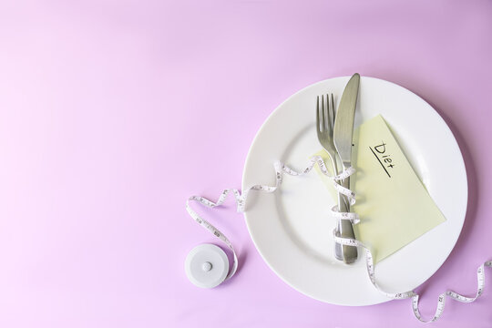 Empty plate, cutlery, measuring tape and a diet note arranged on a pink studio background convey disciplined weight control in a clean banner with copy space