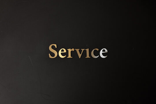 Gold metallic word Service on a dark black wall background. Business customer care, hospitality, help desk, and support concept.