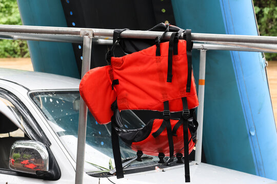 Red life jacket hanging on metal rack above car windshield, bright orange flotation vest with black straps ready for water safety and outdoor adventure