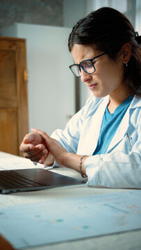 Young Latina female doctor experiencing tendonitis related to prolonged laptop use, representing repetitive strain, workplace discomfort, ergonomics