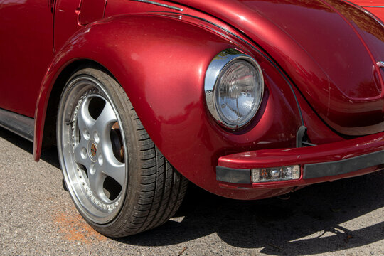 Tavernes Blanques, Spain - June 14, 2026. Detail shot of front round headlight, fender, and custom alloy wheel of retro red Volkswagen Beetle in bright sunlight