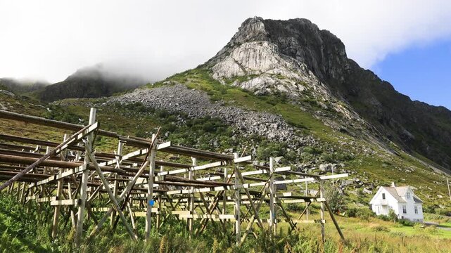View of fish racks in Lofoten, steeply rising mountain landscape above ocean in Norway