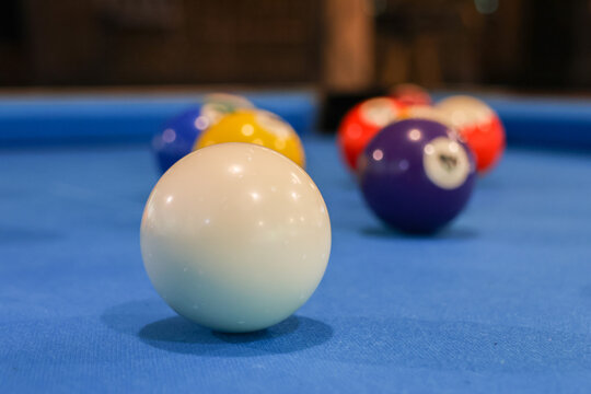 White cue ball on blue felt pool table with colorful billiard ball rack and shallow depth of field creating playful mood