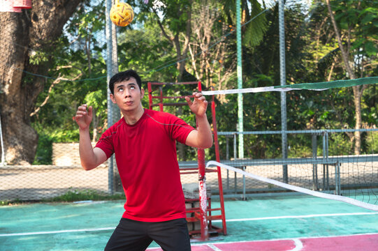 An athletic male Thai sepak takraw player performing a powerful head strike to pass or return the rattan ball during a competitive match on an outdoor court