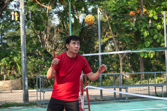 An athletic male Thai sepak takraw player performing a powerful head strike to pass or return the rattan ball during a competitive match on an outdoor court