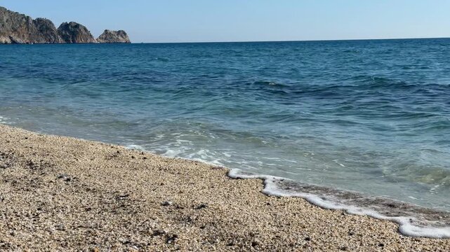 Beach scene with blue sea and island in distance under clear sky. Tranquil and scenic background