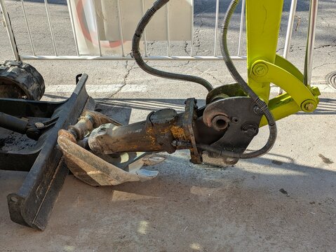 Maquinaria industrial. Vista de cerca del brazo con martillo hidr&aacute;ulico y cubeta de una retroexcavadora color verde aparcada en una zona de obras