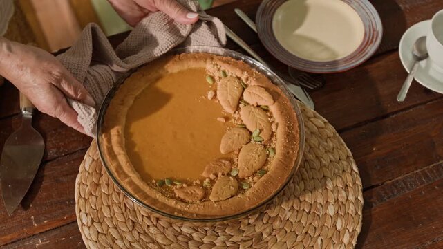 Senior womans hands placing freshly baked pumpkin pie on woven placemat on rustic wooden table, top view. Clip is ideal for Thanksgiving marketing and autumn food promotions