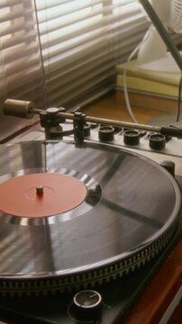 Vertical video of vintage turntable spinning vinyl record. Footage is ideal for retro music promotions, audio equipment advertisements, or nostalgic lifestyle content