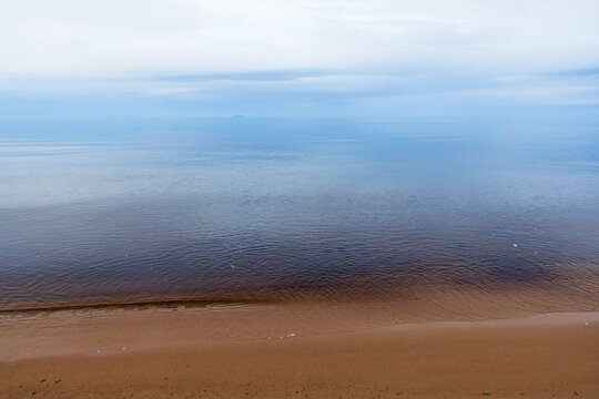 Soft blue lake water meets a quiet sandy shoreline under a pale sky, creating a tranquil, minimalist seascape that conveys calm, solitude, and natural coastal beauty