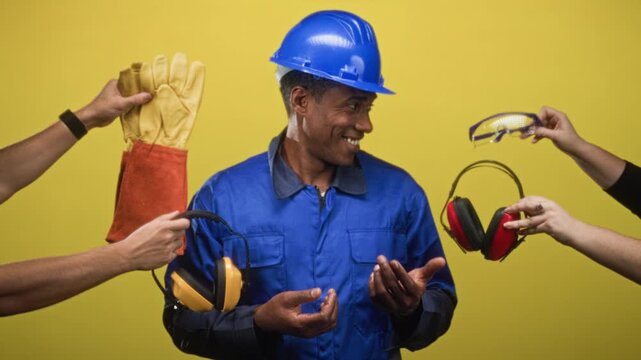 Man in hardhat and blue coverall with palms up while hands offer gloves, earmuffs and safety glasses in studio; safety teamwork pride.