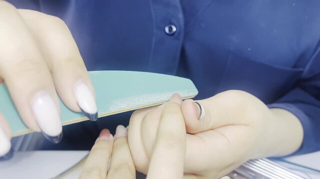 Manicurist filing client nails with nail file close up 16:9, beauty salon manicure treatment concept