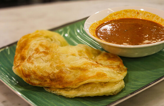 Roti Canai (or Paratha) served with curry on a banana leaf style plate.