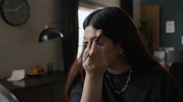Young adult woman dipping brush into palette and applying makeup on her face in front of mirror. Footage is ideal for cosmetics commercials and beauty tutorials