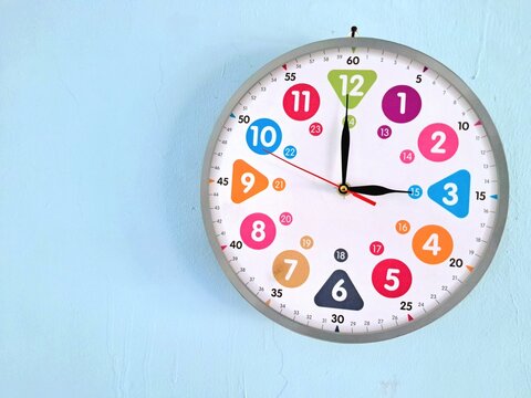 Colorful kids educational wall clock on light blue wall showing three o clock time with copy space.